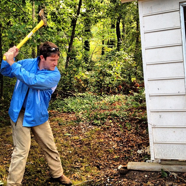 man swinging a sledge hammer at an old junk shed